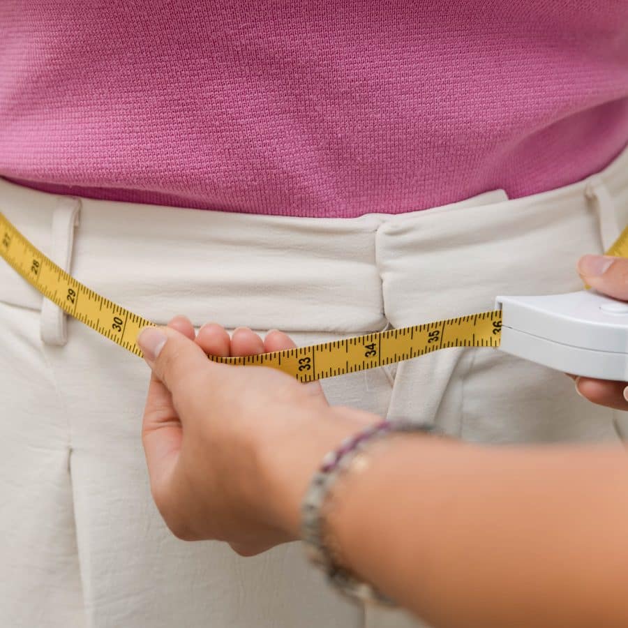 Measuring a woman's waistline with a yellow tape measure for the $200 off GLP-1 weight loss October special in Lakewood Ranch and Bradenton, Florida